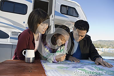 Two parents and daughter looking at map on picnic table outside RV