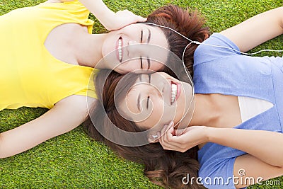 Two pretty young woman lying on grassland and listening music
