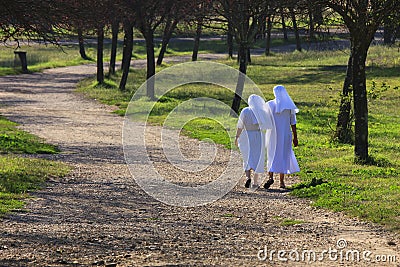 Two sisters (nuns) walking in a park along the path.