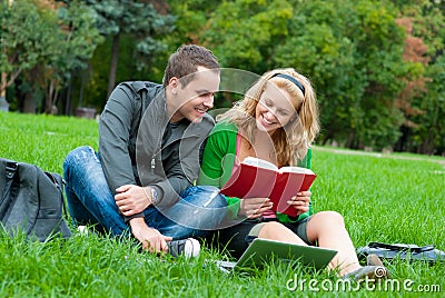 Two students reading a book on the grass