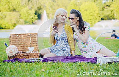 Two women sitting on the blanket and texting