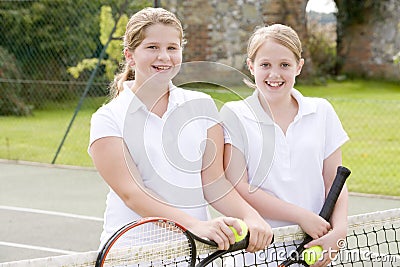 Two young girl friends on tennis court smiling