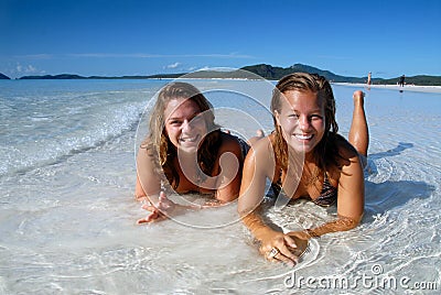 Two young girls in bikini laying in the water