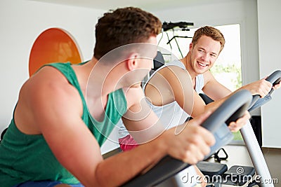 Two Young Men Training In Gym On Cycling Machines Together