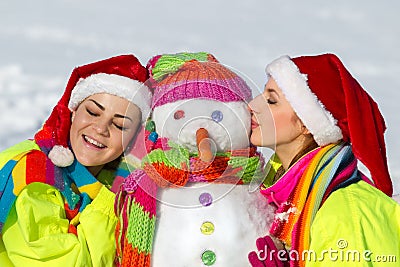 Two young woman kissing a snowman