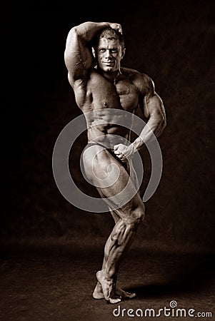 Undressed tanned bodybuilder demonstrates his arms and legs musc
