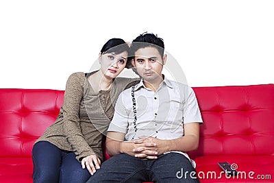 Unhappy couple watching TV and sitting on red sofa