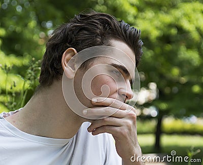 Unhappy, sad young man outdoors in park thinking