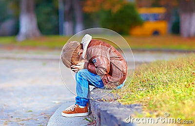 Upset kid boy sitting alone in city park