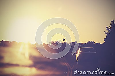 Vintage picture of road with cars in motion against sun.