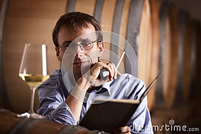 Vintner looking at glass of white wine in cellar.