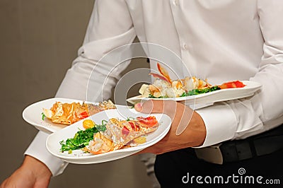 Waiter holds plates with lobsters