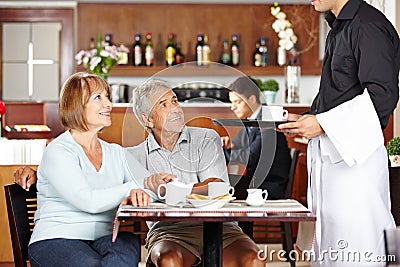Waiter serving seniors in coffee shop