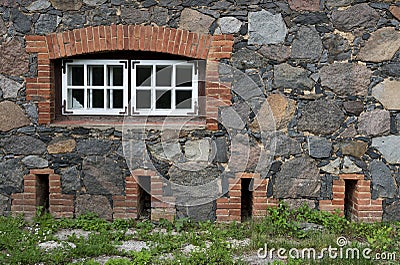 Wall from granite stones with a window and the old road overgr