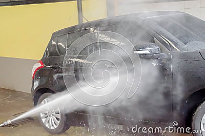 Washing black car by pressure washer gun in car-wash shop