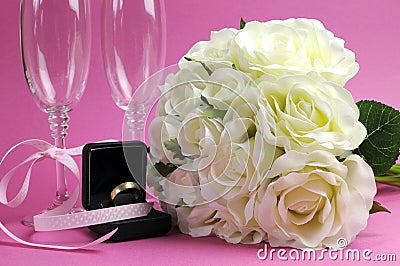 Wedding bridal bouquet of white roses on pink background with pair of champagne flute glasses.