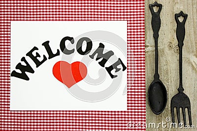 Welcome sign on red checkered tablecloth with cast iron spoon and fork