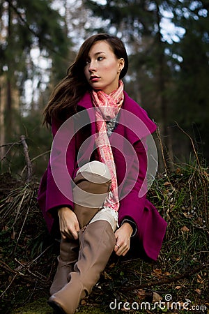 Well-dressed young woman in pink topcoat sitting in forest