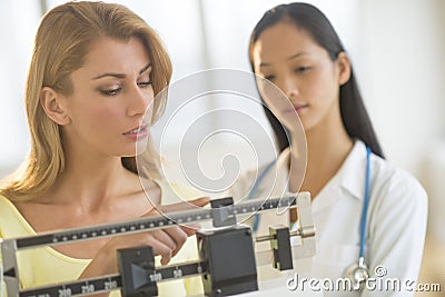 Woman Adjusting Weight Scale While Standing By Female Doctor