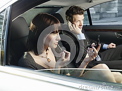 Woman Applying Lip Gloss And Man Using Mobile Phone In Car