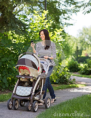 Woman With Baby Carriage Using Cell Phone In Park