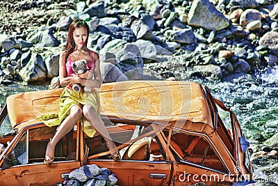 Woman in baby doll stile sitting on a broken car in the sun with teddy bear in hand