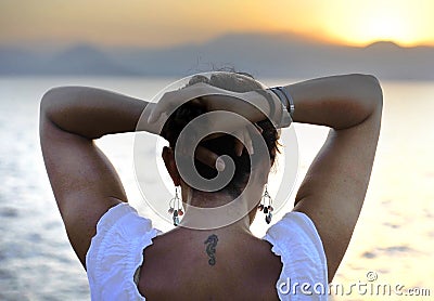 Woman with back seahorse tattoo standing alone looking at sea horizon