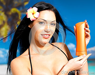 Woman on the beach holds orange sun tan lotion bottle.