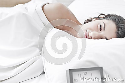 Woman on bed in the morning with a clock ringing