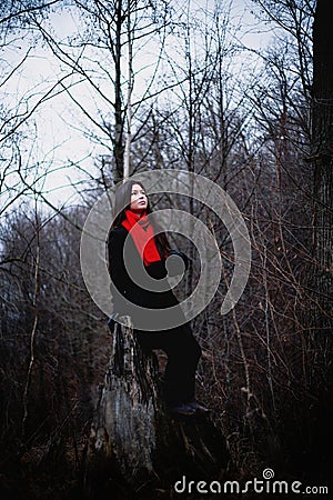 Woman in black coat and red scarf sitting in cold dark forest