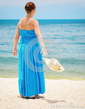 Woman in blue dress throws hat on the beach