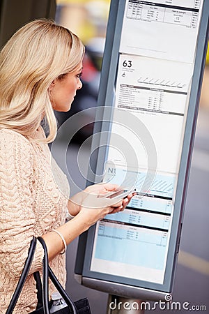 Woman At Bus Stop With Mobile Phone Reading Timetable