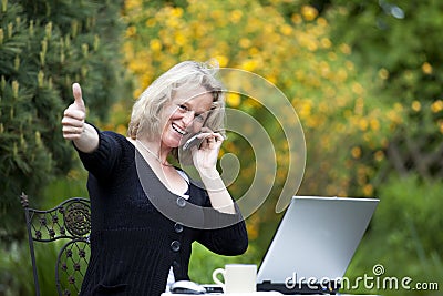 Woman with cellphone and laptop posing thumbs up