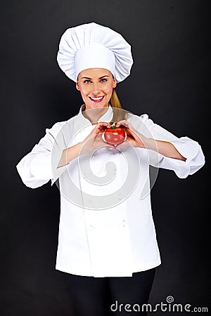 Woman chef make hand heart sign with tomato over dark background