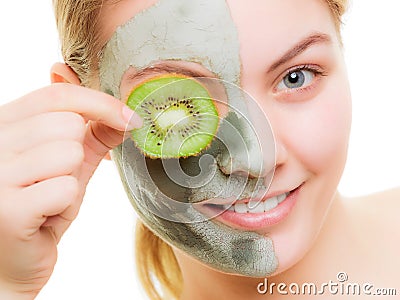 Woman in clay mask on face covering eye with kiwi