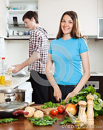 Woman cooking food while man washing dishes