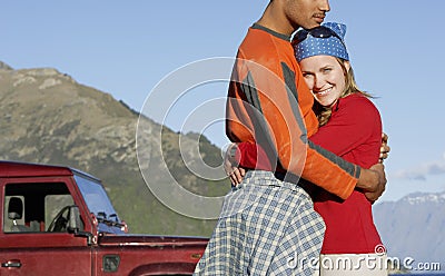 Woman Embracing Man Against Jeep And Mountains