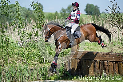 Woman eventer on horse is Drop fence in Water jump