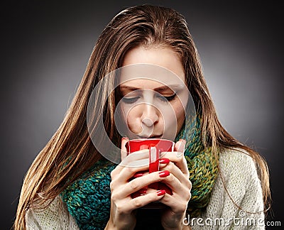 Woman with flu wrapped up in a scarf and drinking hot tea