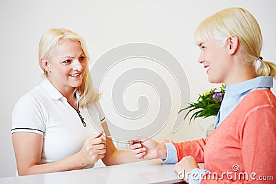 Woman giving health card to doctors assistant