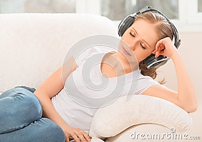Woman in headphones enjoys music while lying on the sofa at home