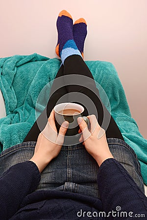 Woman holding a hot drink, relaxing with her feet up