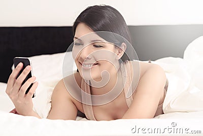 Woman lying in bed reading an sms on her mobile