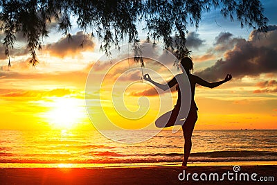 Woman practicing yoga on the beach during a beautiful sunset