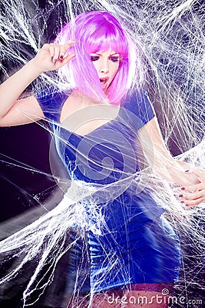 Woman with purple wig and intense make-up trapped in a spider web screaming