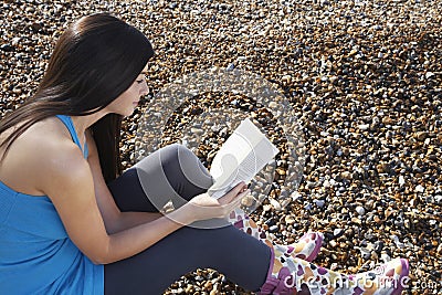 Woman Reading Book While Sitting At Beach