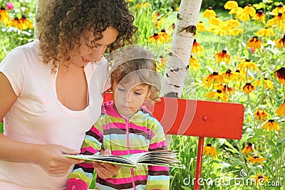 Woman reads book to little girl in garden