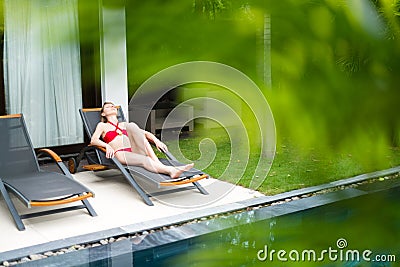 Woman relaxing on chaise longue near pool.