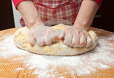 Woman s hands knead dough on wooden table