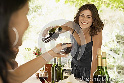 Woman Serving Red Wine To Female Friend In Party